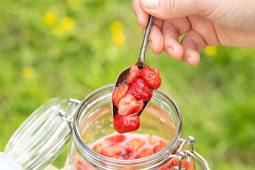 hand die een lepel aardbeien uit glazen pot schept